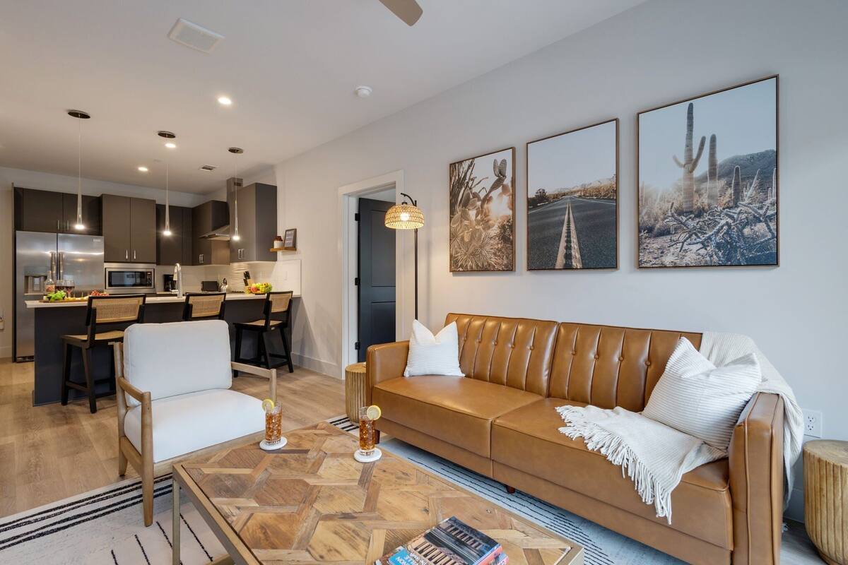 A modern living room with a leather sofa, a coffee table, and a dining area with chairs and a kitchen in the background.