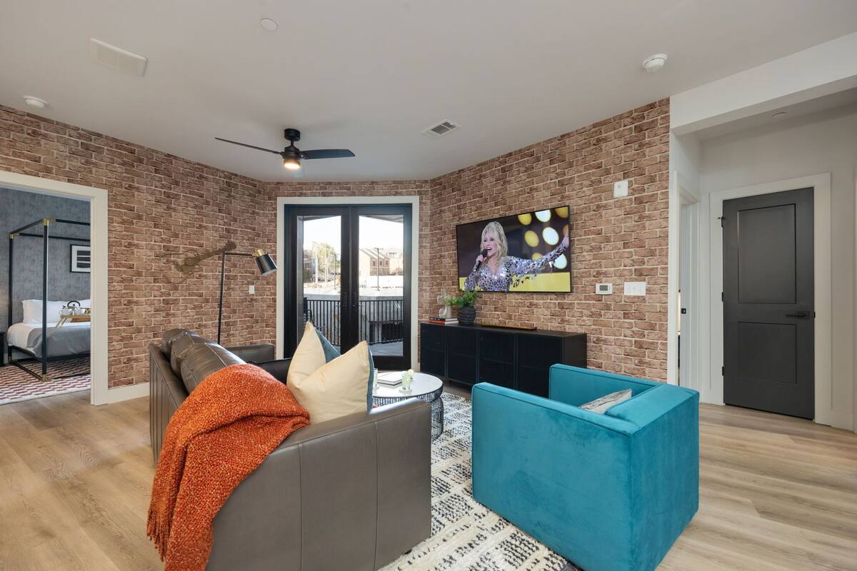 A modern living room with a brick wall, a ceiling fan, a television, and a sofa with a throw blanket.