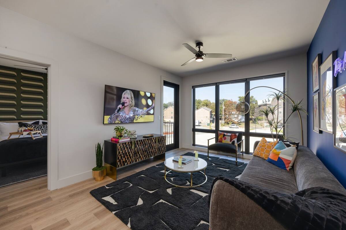 A modern living room with a sofa, coffee table, TV, and large windows.