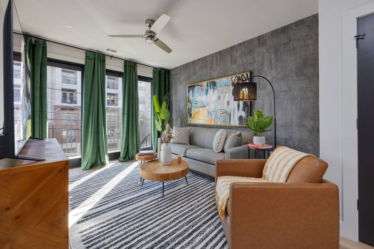 A modern living room with a grey sofa, a brown armchair, a round wooden coffee table, and a striped rug.