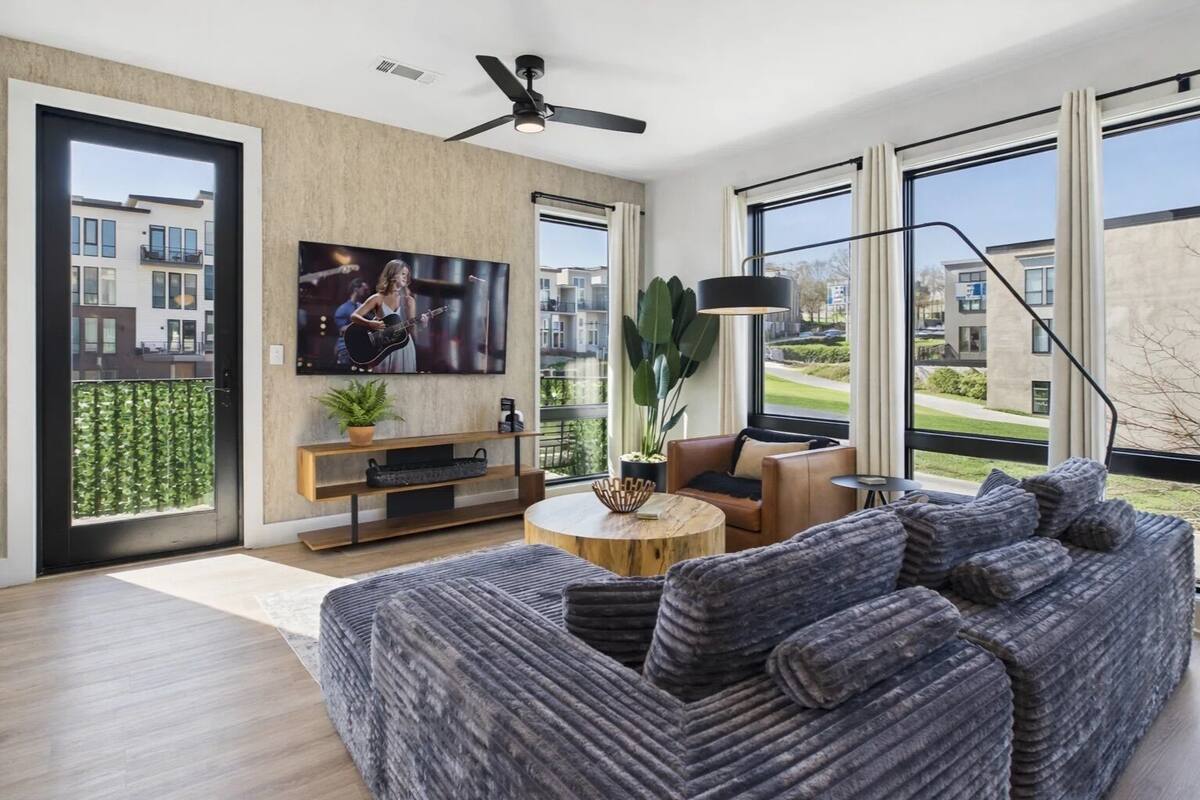A modern living room with a large TV, a ceiling fan, a sofa, a coffee table, and a view of the outside.