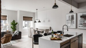 Une cuisine moderne dotée d’un îlot central, de luminaires suspendus et d’un coin repas avec un canapé et une table.