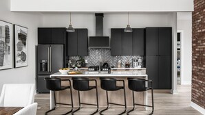 Une cuisine moderne dotée d’un îlot central, de tabourets de bar noirs et d’un mur d’accent en briques.