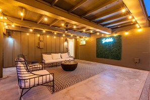 A cozy outdoor seating area with a sofa and chairs, a patterned floor, and string lights.
