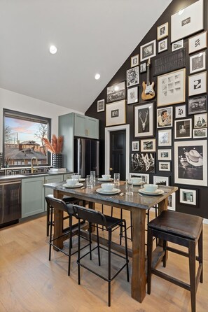 Una cocina moderna con comedor, que presenta una amplia pared de fotografías enmarcadas y vistas a una casa a través de una ventana.