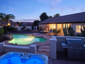 A backyard with a swimming pool, hot tub, and barbecue grill.
