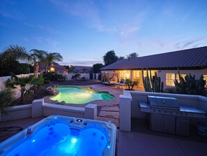A backyard with a swimming pool, hot tub, and barbecue area.