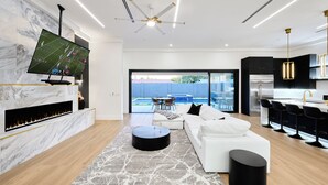 A modern living room with a flat-screen TV, a fireplace, a white sofa, and a view to the outside. - Havana - Walk to Old Town - Heated Pool & Spa (Scottsdale)