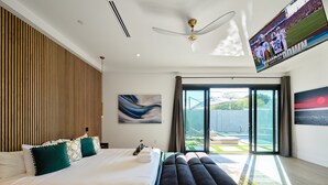 A modern bedroom with a large bed, a bench, a ceiling fan, and a TV displaying a sports game. - Havana - Walk to Old Town - Heated Pool & Spa (Scottsdale)