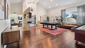 A spacious living room with a pool table, a fireplace, and a large window with patterned curtains. - Kierland Charm - Private Yard w/ Pool, Golf & More (Scottsdale)