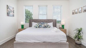 A neatly made bed with a grey headboard, two bedside tables with lamps, and a potted plant. - Verde Heights-sleeps 12-in Cumberland Heights (Nashville)