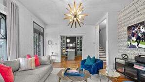 Ein modernes Wohnzimmer mit einem grauen Sofa, einem blauen Sessel und einem Couchtisch. Eine Treppe führt zu einer Küchenzeile.