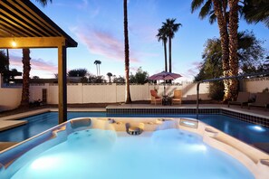 Piscina com hidromassagem, palmeiras e área de estar com cadeiras e guarda-sol.