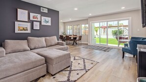 A spacious living room with a grey sectional sofa, a dining area with a table and chairs, and a large sliding glass door leading to a garden. - Desert Rose-hot Tub-pool Heat Avail-fire Pit-golf! (Scottsdale)
