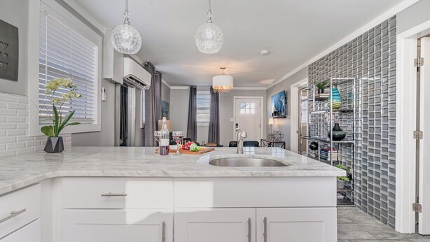 Una cocina moderna con armarios blancos, encimera de mármol e iluminación colgante.