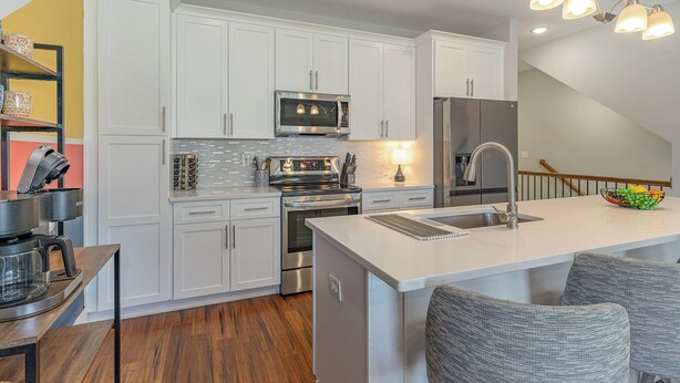 Cocina moderna con armarios blancos, electrodomésticos de acero inoxidable y una isla central con asientos.