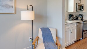 A modern living room with a wooden floor, a blue armchair, a floor lamp, and a kitchen in the background. - Merry Melrose -mins to Broadway- Sleeps 6 (Nashville)