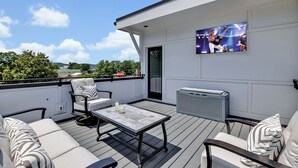 Una terraza en la azotea con televisor de pantalla plana, asientos al aire libre y vistas de la ciudad.