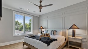 Un dormitorio moderno con una cama grande, mesitas de noche, ventilador de techo y ventana con persianas.