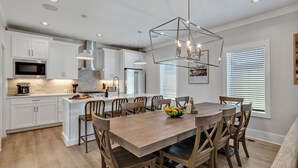 Una cocina moderna con muebles blancos, una isla central y un comedor con sillas y mesa de madera.