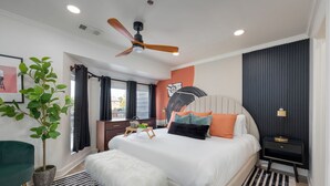 Ein modernes Schlafzimmer mit einem Bett, Deckenventilator, einer Topfpflanze, einem Nachttisch und einem Beistelltisch.