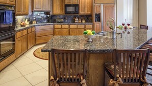 A modern kitchen with wooden cabinets, granite countertops, a central island with bar stools, and built-in appliances. - Valley View Villa - Private Pool - Hidden Bedroom (Scottsdale)