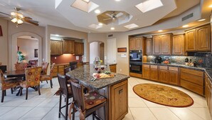 A spacious kitchen with wooden cabinets, a granite countertop, and a dining area with floral chairs. - Valley View Villa - Private Pool - Hidden Bedroom (Scottsdale)