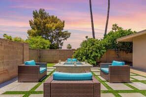 A patio area with wicker furniture, a central table, and a view of trees and a sunset. - Blue Tides Getaway - Private Pool & Fire Pit (Scottsdale)