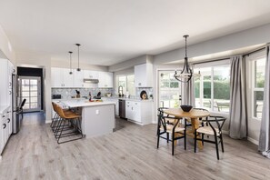 A modern kitchen with white cabinets, a central island, and a dining area with a round table and chairs. - Sereno - Sparkling Pool - Near Scottsdale Quarter (Scottsdale)