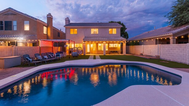 Une maison avec une piscine, un espace extérieur aménagé pour s’asseoir et une terrasse bien éclairée.