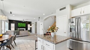 Une cuisine moderne avec des meubles blancs, un réfrigérateur en acier inoxydable et un plan de travail en granit.