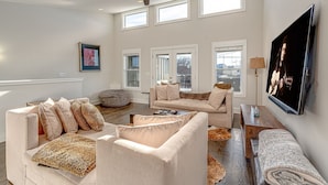 A spacious living room with high ceilings, multiple windows, and a ceiling fan.