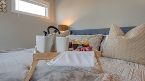 A neatly made bed with a tray of food, a coffee maker, and a lamp on a bedside table.