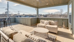 A covered patio with a ceiling fan, a sofa set, a round table, and a bar stool.