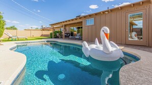 Una piscina con un flotador con forma de cisne, un porche cubierto y un cielo azul despejado.