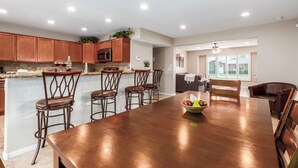 Una cocina moderna con armarios de madera, una isla grande con taburetes de bar y una zona de comedor con mesa y sillas de madera.