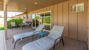 Un patio techado con dos sillones de descanso, una mesita y un ventanal corredizo que da a un jardín trasero.