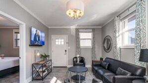 A modern living room with a sofa, a coffee table, a TV mounted on the wall, and a door leading to another room. - Opulent Pearl - Private Patio - Mins to Broadway (Nashville)