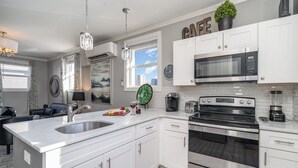A modern kitchen with white cabinets, stainless steel appliances, a large island with a sink, and a dining area with a black leather couch. - Opulent Pearl - Private Patio - Mins to Broadway (Nashville)