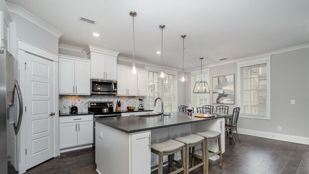 A modern kitchen with white cabinets, a central island with bar stools, a microwave, and pendant lighting.