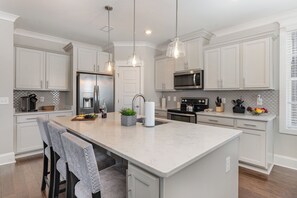 Una cocina moderna con armarios blancos, una isla central, iluminación colgante y electrodomésticos de acero inoxidable.