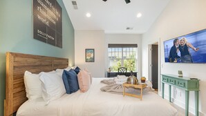 A bedroom with a large bed, a wooden headboard, a television, and a window with a view of greenery.