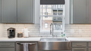 A modern kitchen with grey cabinets, a stainless steel sink, a coffee maker, and a window with a view of a building.