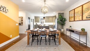 A modern kitchen with a central island, wooden dining table with chairs, and a hanging light fixture.