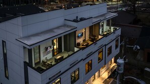 A modern building with a rooftop terrace featuring outdoor seating and a TV screen. - Heart of Gulch - 4 Min to Broadway - Designer Home (Nashville)
