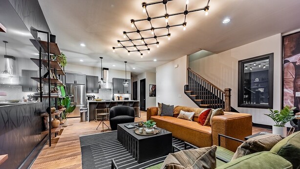 A modern living room with a sofa, coffee table, and a staircase leading to a dining area. - Heart of Gulch - 4 Min to Broadway - Designer Home (Nashville)