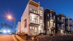 Un edificio residencial moderno de varios pisos, con balcones, un muro de contención de piedra y una calle bien iluminada.