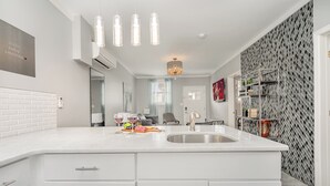 A modern kitchen with white cabinetry, a large island with a sink, pendant lights, and a patterned backsplash. - Lucent Pearl - Private Patio - Near Broadway (Nashville)