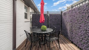 A patio with a round table and chairs, surrounded by a wooden deck and a purple flower wall. - Lucent Pearl - Private Patio - Near Broadway (Nashville)