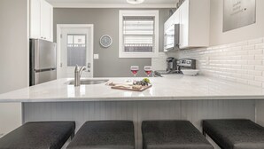 A modern kitchen with a central island, bar stools, a refrigerator, and a clock on the wall. - Lucent Pearl - Private Patio - Near Broadway (Nashville)